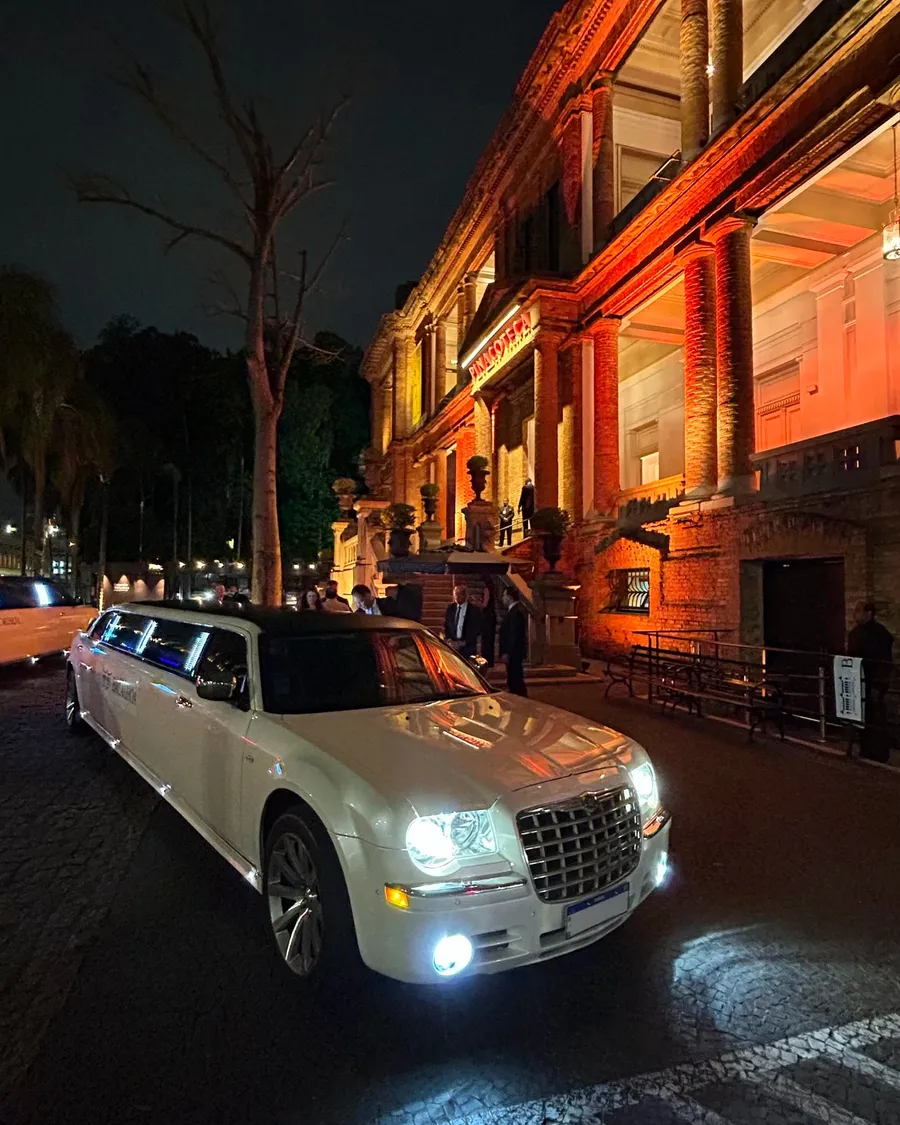 Limousine Chrysler 300C branca à noite, com os faróis acesos, em frente a um prédio histórico iluminado